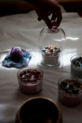a woman uses a glass lid to protect a candle decorated with semi-precious stones. A ray of light...