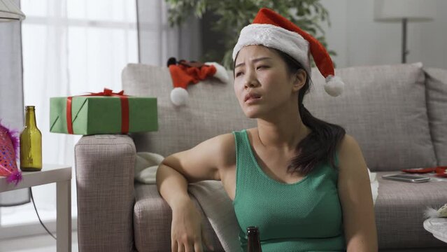 portrait of chinese lady wearing party hat and obsessed with drinking waking up in her apartment. asian degenerate girl holding beer bottle is looking around the surrounding with dreamy eyes.