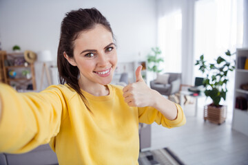 Photo of confident blogger lovely cute lady raise thumb up take selfie wear yellow pullover comfortable home indoors