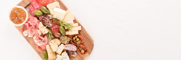 Italian antipasti board with variety of cheeses, sausages served with sun dried tomatoes, olives, jams and herbs on white table - parmesan, dorblu, prosciutto, salami.  Menu banner with copy space