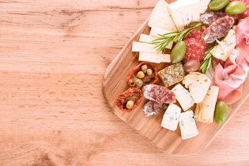 Top view on Italian antipasti board with variety of cheeses, sausages served with sun dried tomatoes, olives, jams and herbs on wooden table - parmesan, prosciutto.  Menu background with copy space