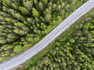 Bird's eye view of a forest road, no cars. Aerial, drone nature photography taken from above in Sweden in summer. Surroundings with coniferous trees. Copy space. Travel and transportation concept. © Anna