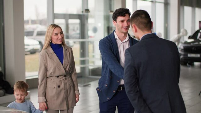 auto shop, young happy family with male child in their arms meets with a manager to choose new car in dealership