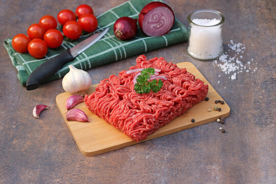 Rohes Hackfleisch auf einem Holzbrett mit Tomaten ,Knoblauch und Zwiebeln.