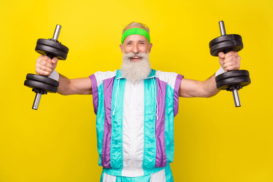 Photo of positive satisfied aged person hands hold dumbbells wear condensed milk tin color sport suit isolated on yellow background