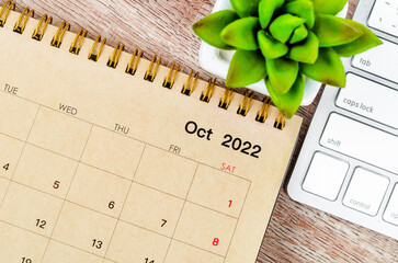 October 2022 desk calendar with keyboard computer on wooden background.
