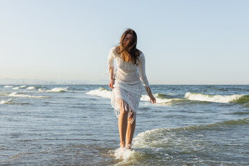 Brunette woman in dress standing in sea water.