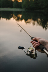 Man catching fish, pulling rod while fishing from lake or pond. Fisherman with rod, spinning reel on a boat. Sunrise. Fishing for pike, and perch. Background wild nature.