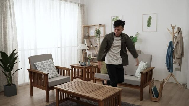 slow motion of an active asian male enjoying pop dancing in the living room at home with wood furniture during daytime.