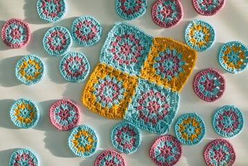 Top view of multicolored crochet motifs - one big square and  many small circles on white surface with rough texture, bold shadows in hard light. - obrazy, fototapety, plakaty