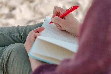 Person seated on the beach taking notes in the diary