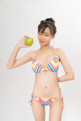 Naklejka premium Portrait of a young and attractive sexy asian female lady model wearing colorful summer bikini holding a green apple, good for health or dietary concept