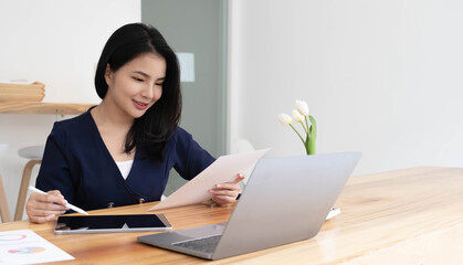 Young asian businesswoman works on tablet with laptop at the office.