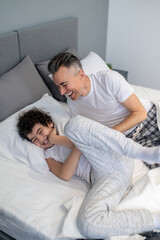 Father and son having fun in bed in the morning and looking joyful