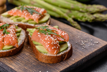 Toast sandwich with butter, avocado and salmon, decorated with arugula and sesame seeds, on a black stone background