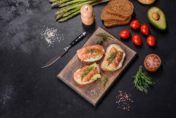 Toast sandwich with butter, avocado and salmon, decorated with arugula and sesame seeds, on a black stone background