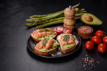 Toast sandwich with butter, avocado and salmon, decorated with arugula and sesame seeds, on a black stone background