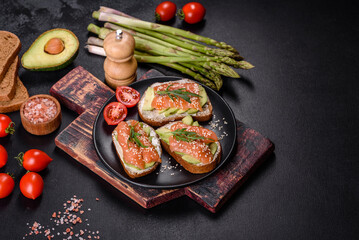 Toast sandwich with butter, avocado and salmon, decorated with arugula and sesame seeds, on a black stone background