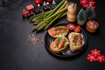 Toast sandwich with butter, avocado and salmon, decorated with arugula and sesame seeds, on a christmas table