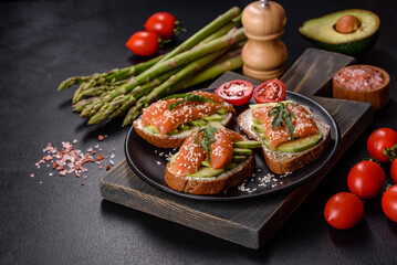 Toast sandwich with butter, avocado and salmon, decorated with arugula and sesame seeds, on a black stone background