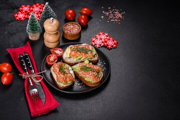 Toast sandwich with butter, avocado and salmon, decorated with arugula and sesame seeds, on a christmas table