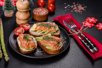 Toast sandwich with butter, avocado and salmon, decorated with arugula and sesame seeds, on a christmas table