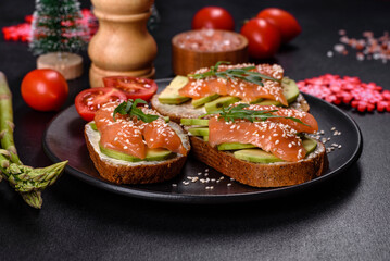 Toast sandwich with butter, avocado and salmon, decorated with arugula and sesame seeds, on a christmas table