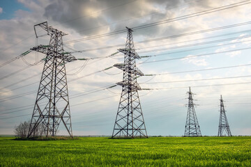 High voltage lines and power pylons in a flat and green agricultural landscape on a sunny day with clouds in the blue sky. Cloudy and rainy. Wheat is growing