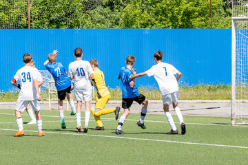 Children's football for boys aged 13-14. Active dynamic struggle for the ball between young men from the opposing teams on the green football field.