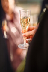 New Year's blurred festive background with a man's hand with a glass of champagne and bokeh from fireworks. wedding champagne party. the groom in a suit holds a glass of champagne in his hand. blurry