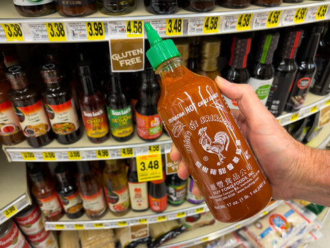 ATLANTA, GEORGIA - June 16, 2022 : Person holding Sriracha hot chili sauce bottle at an American grocery store supermarket. Sriracha is produced by Huy Fong Inc., one of the world's largest producers 