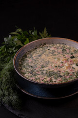 summer okroshka soup in a bowl on a black background next to the greens