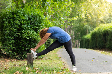 Mature female in activewear doing exercise for leg stretch while enjoying workout in natural environment