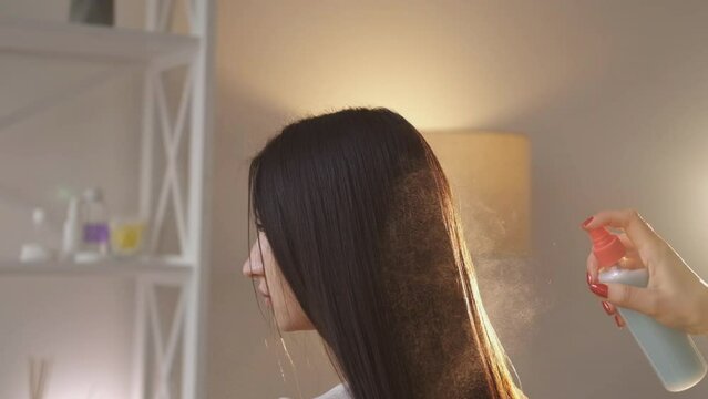 Beauty salon. Female hairstyle. Treatment cosmetic. Unrecognizable hairdresser spraying smooth careful long brunette hair of woman in light room interior slow motion.