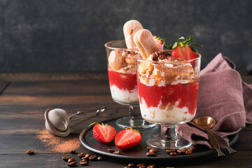 Strawberry tiramisu. Traditional Italian dessert tiramisu in glass with fresh strawberry and mint leaves on old wooden dark table background. Copy space. Food background.