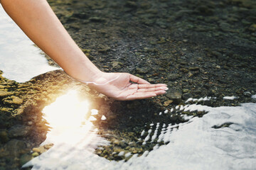 Man's hand touching water in the midst of nature