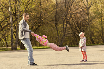 Dad plays with his daughters in the park. Twirling a girl around. Family