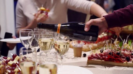Waiter pouring glasses with champagne on catering service on banquet table with canape snacks in restaurant or hotel. Food set on birthday, wedding celebration or business conference event venue. - Powered by Adobe