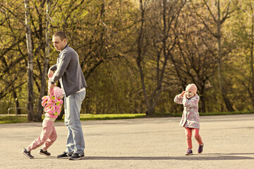 Fototapeta premium Dad plays with his daughters in the park. Twirling a girl around. Family