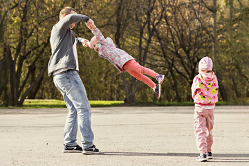 Obraz premium Dad plays with his daughters in the park. Twirling a girl around. Family