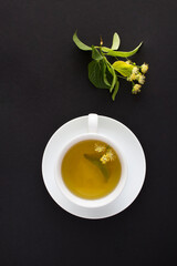 Tea with linden flower in the white cup on the black background. Top view. Copy space.