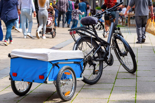 Black bicycle with small covered blue trailer parked in a shopping streetBicycle with small trailer parked in a shopping street