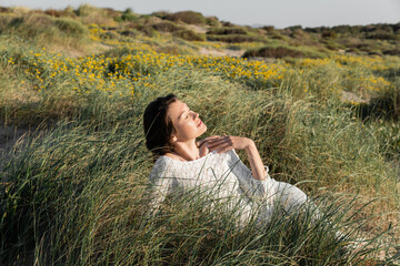 Naklejka na ściany i meble Woman in summer dress relaxing on grass on beach.