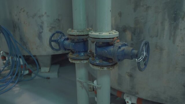 Valves attached to the pipes at the industrial factory. Valves control the flow of liquid entering storage tanks at the industrial factory. Old Blue valves connected to industrial factory equipment.