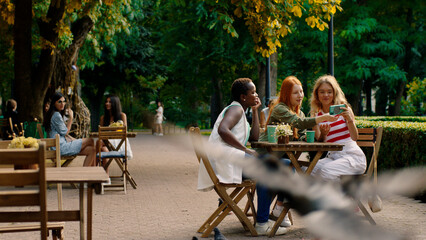 Amazing group of young females have a great time together at the patisserie they are discussing together African lady showing something on her smartphone