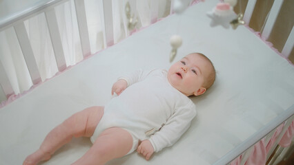 Cute little baby girl in her baby cot playing alone while looking up to the cot toys concept of childhood and health