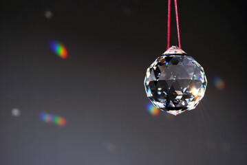 Faceted Feng Shui Crystal ball haning on a red string reflecting the sunlight in little rainbows on the dark wall on the background. Horizontal.