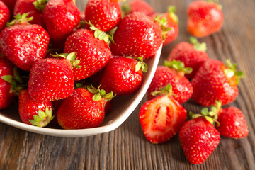 Red strawberry in a white plate on a brown wooden background
