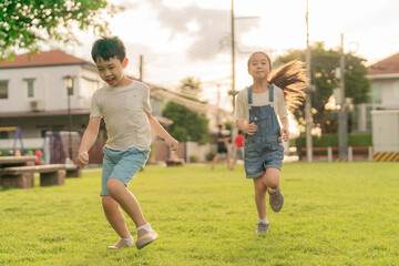 Boy and girl running together with smile in the public garden on sunset time. Children playful run on green meadow. Kid friendship happy childhood. Selective focus on boy. Spend time with nature