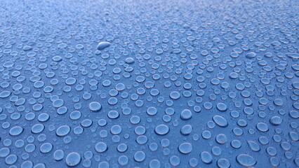 Abstract background. Large drops of rain on the light blue roof of the car.